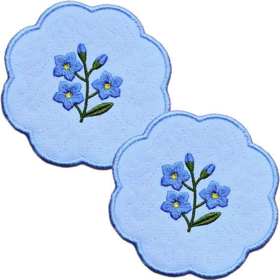Set of two embroidered forget me not candle coasters with blue flower sprigs, soft textured backgrounds and blue scalloped borders.