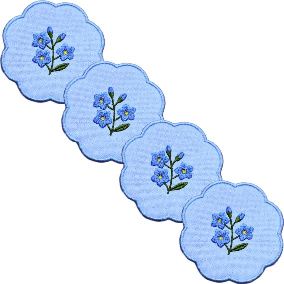 Set of four embroidered forget me not candle coasters arranged diagonally, each with blue flower sprigs and soft blue scalloped borders.