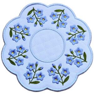 Close up of an embroidered forget me not candle mat with blue flowers, green stems and leaves arranged around a circular centre with a soft scalloped border.