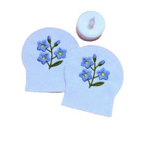Two embroidered forget me not tealight covers made from white felt, shown with an LED tealight for display.