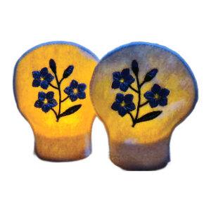 Two lit forget me not tealight covers glowing warmly over LED tealights, with embroidered blue flowers on white felt.