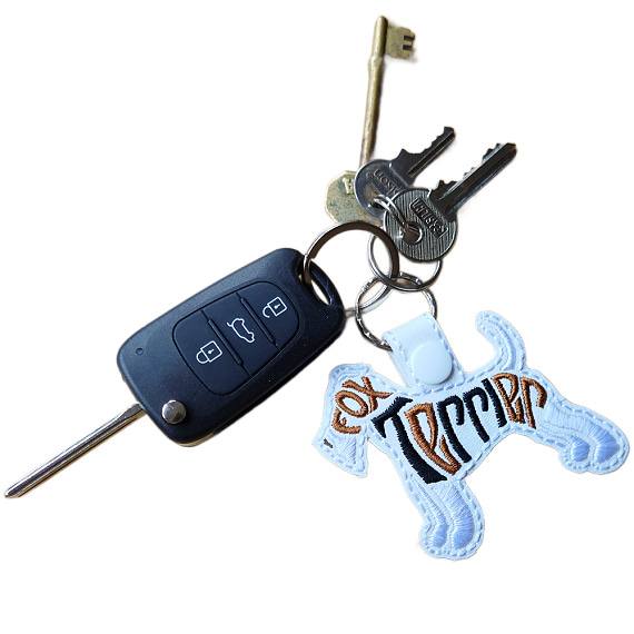 White embroidered Fox Terrier word art keyring attached to a set of keys, showing how it looks in everyday use.
