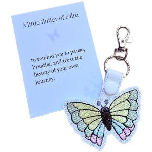 White faux leather butterfly keyring with pastel embroidered wings, shown with a matching keepsake card about calm and trusting your journey.
