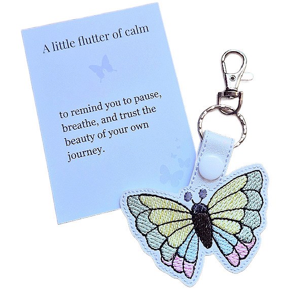 White faux leather butterfly keyring with pastel embroidered wings, shown with a matching keepsake card about calm and trusting your journey.