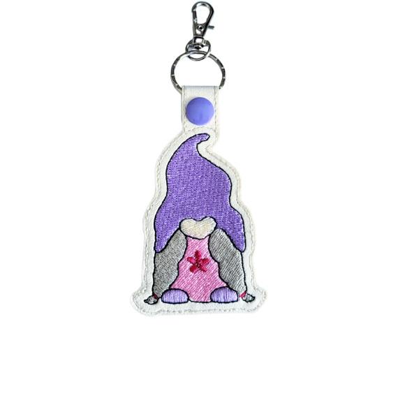 Embroidered girl gnome keyring in faux leather, featuring a purple hat, pink dress, grey hair and sturdy metal keyring hardware.