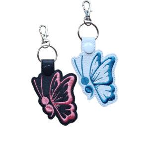 Black and white faux leather butterfly keyrings with embroidered wing outlines and silver metal lobster clasps.