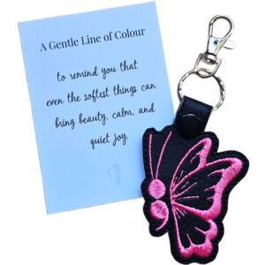 Black faux leather butterfly keyring with pink embroidered wing detail, shown with a matching keepsake card about beauty, calm and quiet joy.