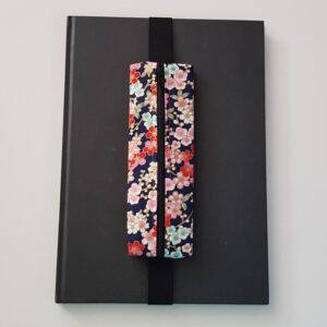 Handmade A4 planner zipper pouch in cherry blossom print cotton fabric, shown fitted around a black A4 notebook with a black zip and black elastic strap, holding pens and stationery items.