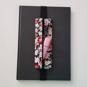 Handmade A4 planner zipper pouch in cherry blossom print cotton fabric, shown fitted around a black A4 notebook with a black zip and black elastic strap, holding pens and stationery items.