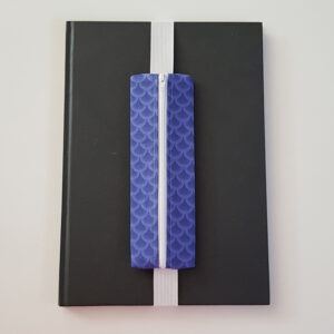Handmade A4 planner zipper pouch in blue mermaid scale print cotton fabric, shown fitted around a black A4 notebook with a white zip and white elastic strap, holding pens and stationery items.