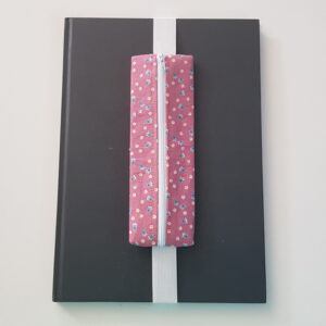 Handmade A4 planner zipper pouch in pink ditsy flower print cotton fabric, shown fitted around a black A4 notebook with a white zip and white elastic strap, holding pens and stationery items.