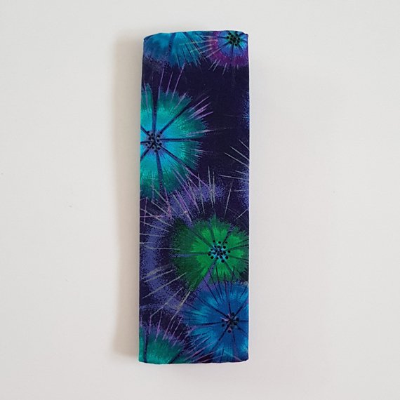 Handmade A5 planner zipper pouch in blue, turquoise and purple tie dye print cotton fabric, shown fitted around a navy A5 notebook with a black zip and black elastic strap, holding pens and stationery items.