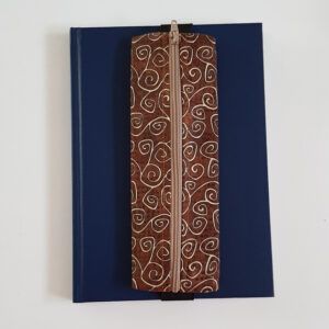 Handmade A5 planner zipper pouch in brown cotton fabric with a cream swirl print, shown fitted around a navy A5 notebook with a matching zip and black elastic strap, holding pens and stationery items.