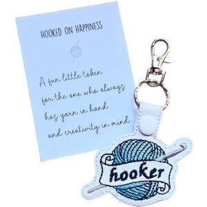 Embroidered Happy Hooker crochet keyring on a matching keepsake card, featuring a yarn ball, crochet hook and playful stitched wording.