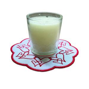 Embroidered heart candle mat with flowing red heart designs around the edge, shown with a glass candle in the centre.