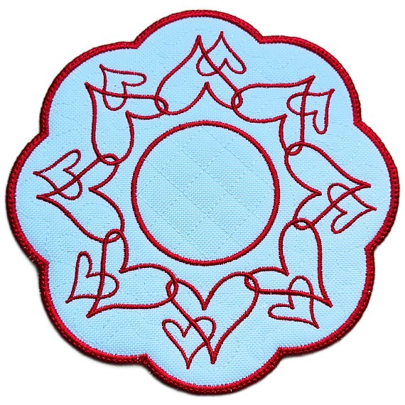 Close up of an embroidered heart candle mat with flowing red heart designs, circular centre and rich red scalloped border.
