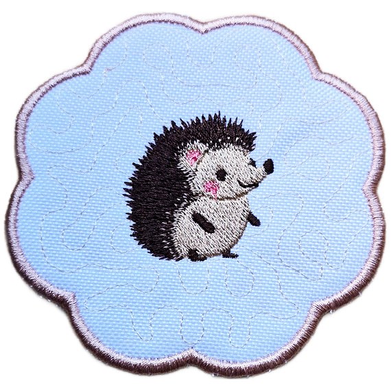 Close up of an embroidered hedgehog candle coaster with a cute stitched hedgehog in the centre, scalloped edging and soft stitched background detail.