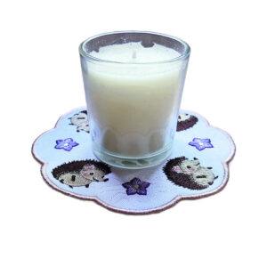 Embroidered hedgehog candle mat with four cute hedgehogs and stitched flower details, displayed under a glass jar candle.