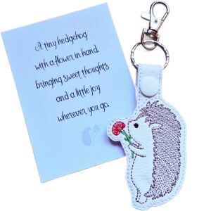 Embroidered hedgehog keyring holding a red flower, shown beside a matching keepsake card with a sweet hedgehog gift message.