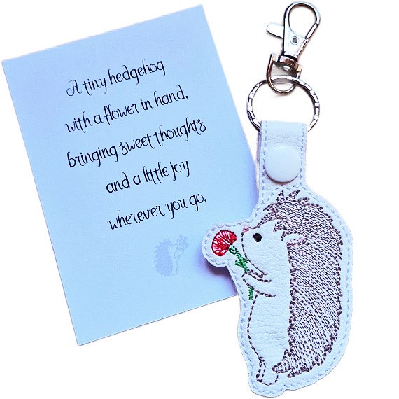 Embroidered hedgehog keyring holding a red flower, shown beside a matching keepsake card with a sweet hedgehog gift message.