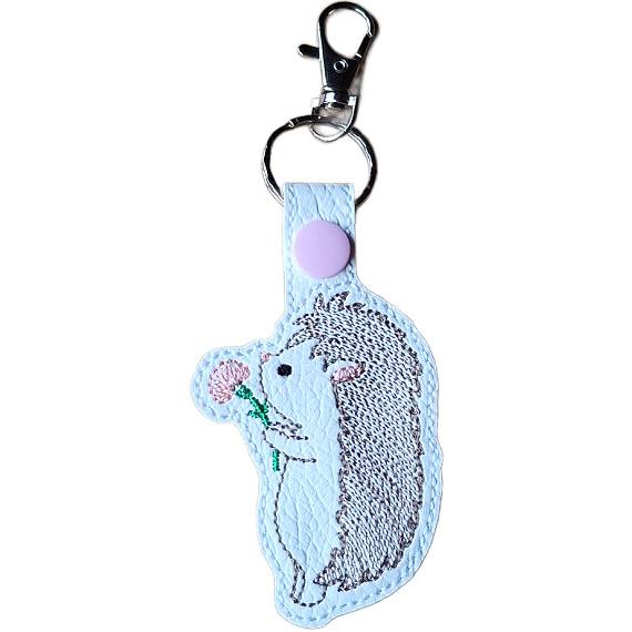 Embroidered hedgehog keyring in faux leather, featuring a cute hedgehog holding a pink flower with sturdy metal keyring hardware.