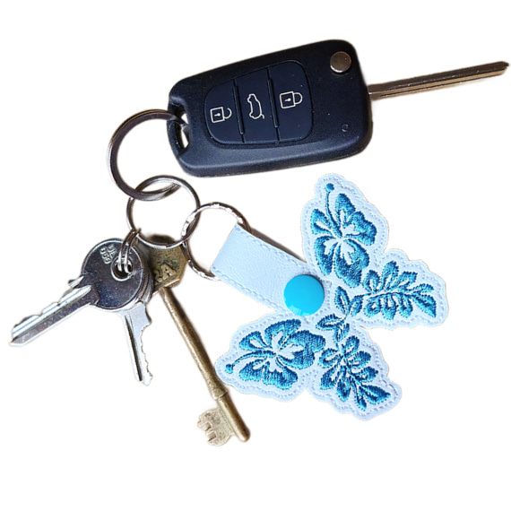 White faux leather hibiscus butterfly keyring attached to a set of keys, showing its size and everyday use.