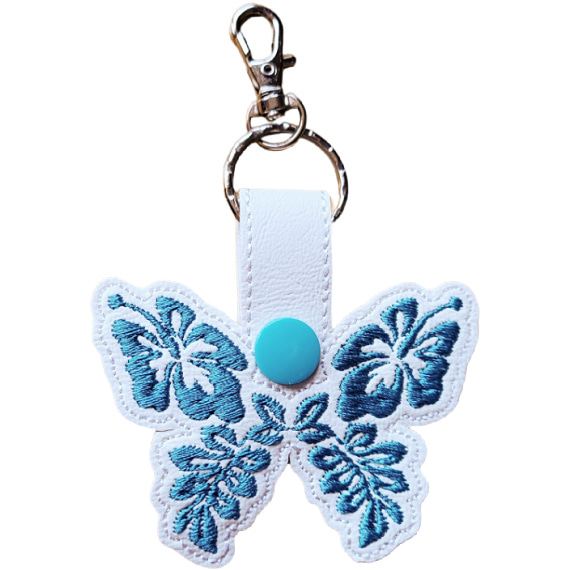White faux leather hibiscus butterfly keyring with teal floral embroidered wings, turquoise snap and silver metal clasp.