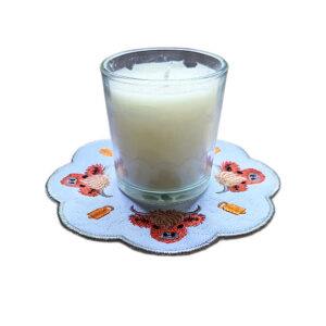 Embroidered Highland cow candle mat with sweet stitched Highland cows, rustic decorative details, scalloped edging and a glass jar candle displayed in the centre.