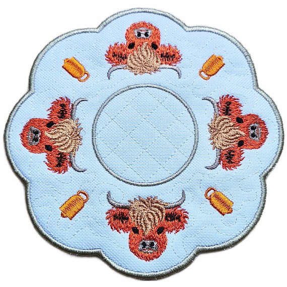Close up of an embroidered Highland cow candle mat showing four stitched Highland cows, small mug details, scalloped edging and a central circle for a candle or display item.