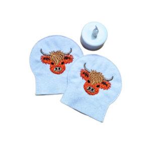 Set of two embroidered Highland cow tealight covers made from soft felt, shown with an LED tealight for a cosy farmhouse display.