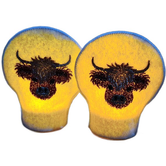 Set of two embroidered Highland cow tealight covers made from soft felt, shown with an LED tealight for a cosy farmhouse display.