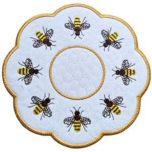Close up of an embroidered honey bee candle mat with a golden scalloped border, stitched honeycomb background and detailed bees arranged around the centre.