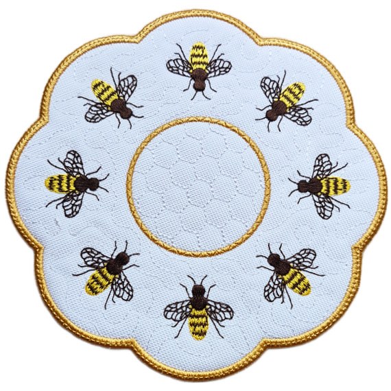 Close up of an embroidered honey bee candle mat with a golden scalloped border, stitched honeycomb background and detailed bees arranged around the centre.