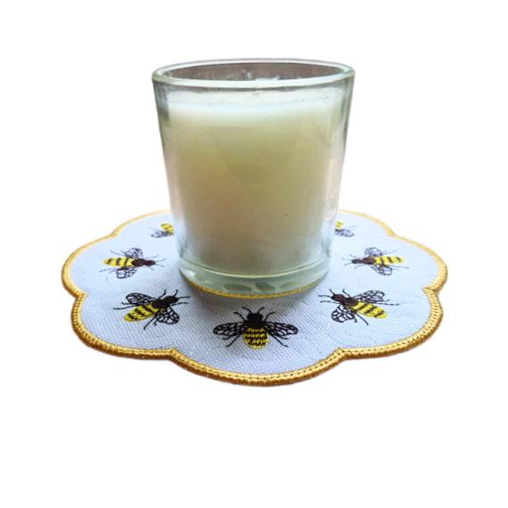 Embroidered honey bee candle mat with a scalloped golden border, shown underneath a glass candle jar with stitched bees around the edge.