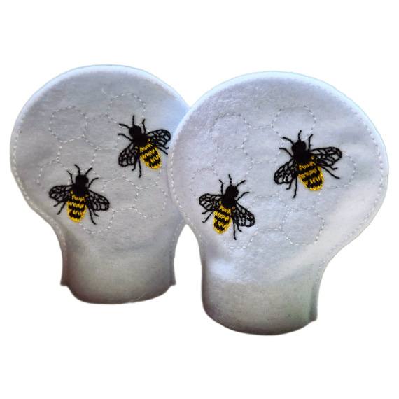 Unlit embroidered honey bee tealight covers on white felt, with stitched bees and honeycomb detail designed to fit over battery operated LED tealights.