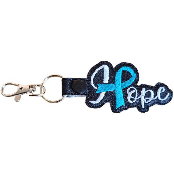 Embroidered Hope ribbon keyring made from black faux leather, featuring white stitched wording, a teal awareness ribbon detail and silver metal hardware.
