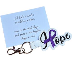 Embroidered Hope ribbon keyring made from white faux leather, shown with a keepsake card featuring a message about holding on to hope and brighter days ahead.
