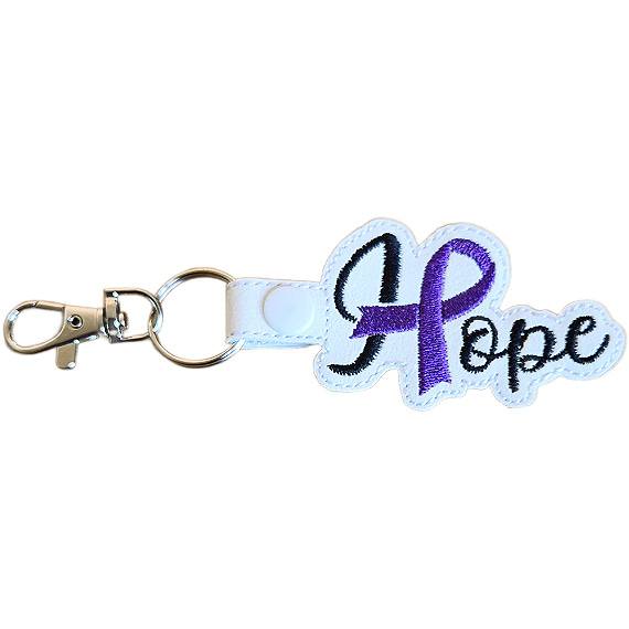 Embroidered Hope ribbon keyring made from white faux leather, featuring black stitched wording, a purple awareness ribbon detail and silver metal hardware.