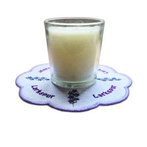 Embroidered July birth flower candle mat with purple larkspur stems, stitched text and a scalloped purple border, shown underneath a glass candle jar.
