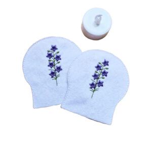 Embroidered July birth flower tealight covers on white felt, with purple larkspur stems and green stitched detail, shown beside a battery operated LED tealight.