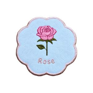 Embroidered June birth flower candle coaster with a pink rose, green leaves, stitched rose text and a softly scalloped border.