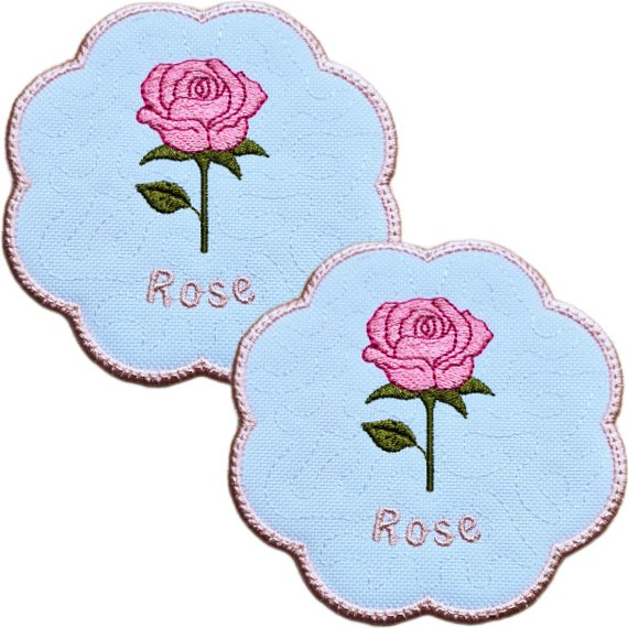 Set of two embroidered June birth flower candle coasters, each with a pink rose, green leaves, stitched rose text and a softly scalloped pink border.