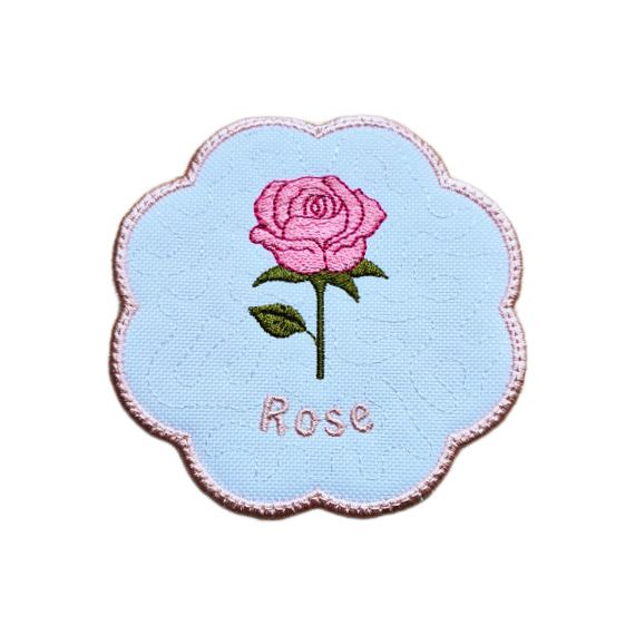 Embroidered June birth flower candle coaster with a pink rose, green leaves, stitched rose text and a softly scalloped border.