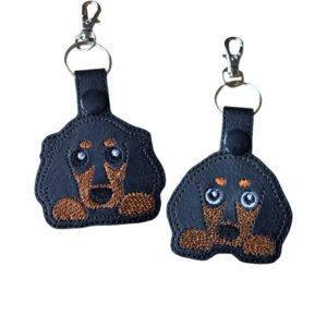Two black Kawaii Dachshund keyrings showing short-haired and long-haired sausage dog designs with embroidered details and silver metal hardware.