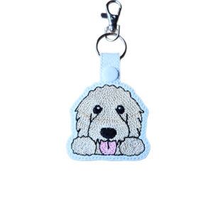 Kawaii Goldendoodle keyring made from white faux leather, with embroidered fluffy face, sweet paws, pink tongue and silver metal hardware.