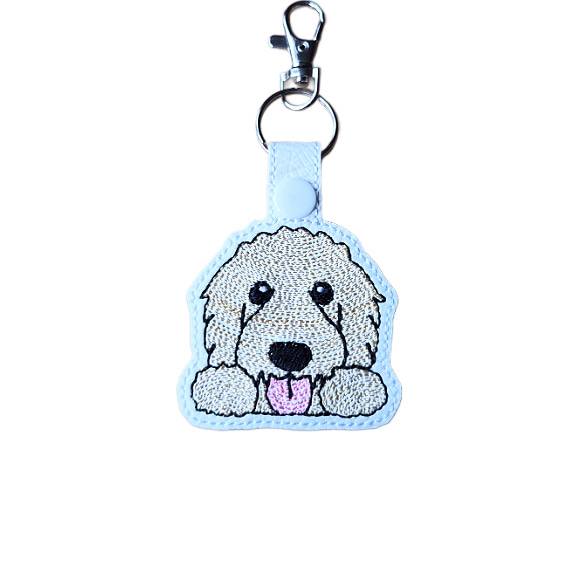 Kawaii Goldendoodle keyring made from white faux leather, with embroidered fluffy face, sweet paws, pink tongue and silver metal hardware.