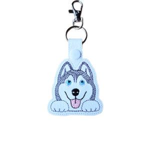 Kawaii Husky keyring made from white faux leather, with embroidered blue eyes, fluffy face, sweet paws, pink tongue and silver metal hardware.
