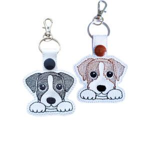 Two Kawaii Jack Russell Terrier keyrings in black and white and brown and white designs, shown with embroidered details and silver metal hardware.
