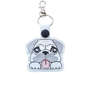 Kawaii Pug keyring made from white faux leather, with embroidered floppy ears, wrinkly face, pink tongue and silver metal hardware.