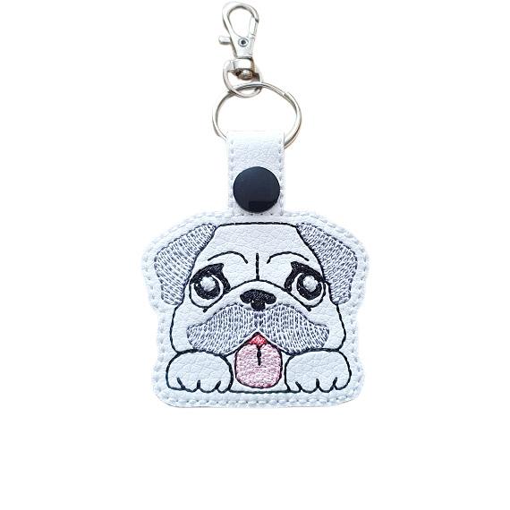 Kawaii Pug keyring made from white faux leather, with embroidered floppy ears, wrinkly face, pink tongue and silver metal hardware.